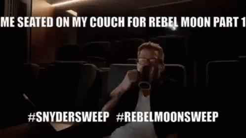 A Man Is Sitting On A Couch Drinking From A Cup In A Theater . GIF