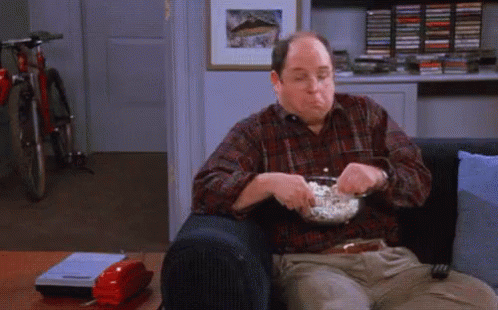 A Man Is Sitting On A Couch Eating Popcorn And Watching Tv . GIF