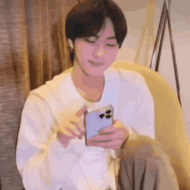 A Man Is Sitting On A Couch Holding A Cell Phone In His Hand . GIF