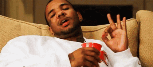 A Man Is Sitting On A Couch Holding A Cup Of Coffee And Making An Ok Sign . GIF