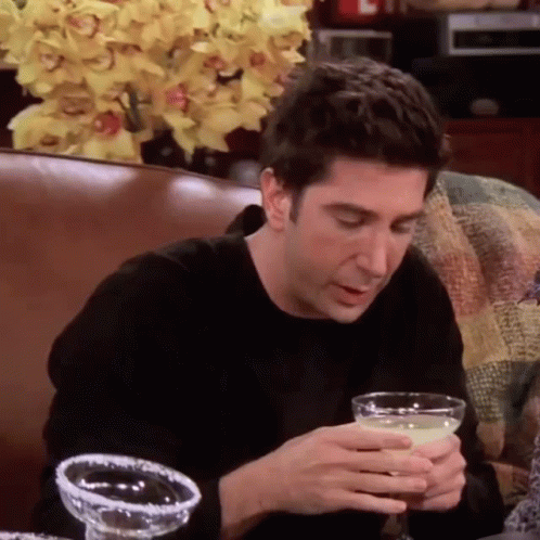 A Man Is Sitting On A Couch Holding A Margarita In His Hand . GIF
