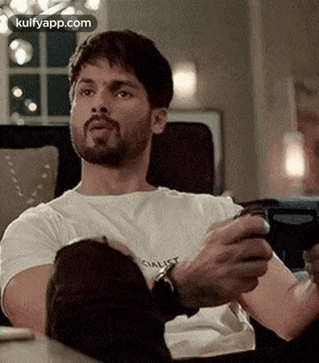 A Man Is Sitting On A Couch Holding A Remote Control . GIF