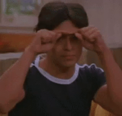 A Man Is Sitting On A Couch Holding His Hands To His Eyes . GIF