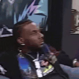 A Man Is Sitting On A Couch In Front Of A Wall With A Picture On It . GIF
