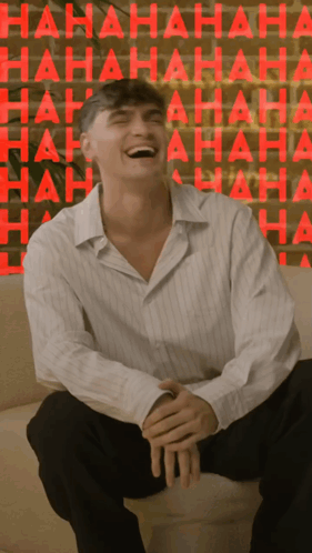 A Man Is Sitting On A Couch Laughing In Front Of A Wall That Says ' Hahaha ' GIF