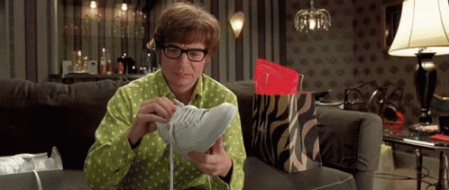A Man Is Sitting On A Couch Looking At A Pair Of Shoes GIF