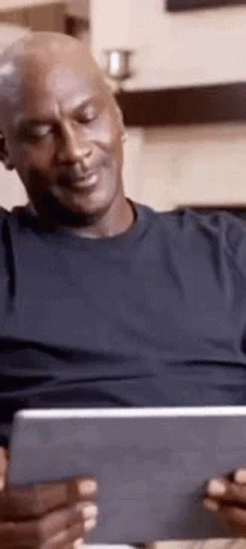 A Man Is Sitting On A Couch Looking At A Tablet Computer . GIF