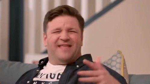 A Man Is Sitting On A Couch Making A Funny Face While Laughing . GIF