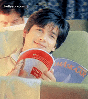 A Man Is Sitting On A Couch Reading A Book And Smiling . GIF