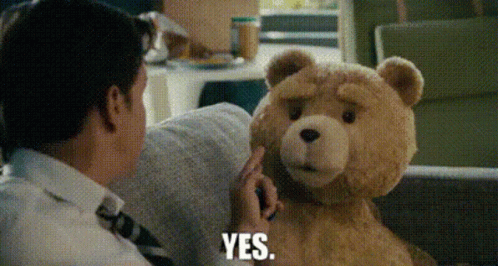 A Man Is Sitting On A Couch Talking To A Teddy Bear Who Is Saying Yes GIF