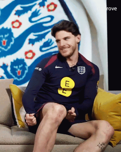 A Man Is Sitting On A Couch Wearing A Blue Nike Shirt With The Letter E On It GIF