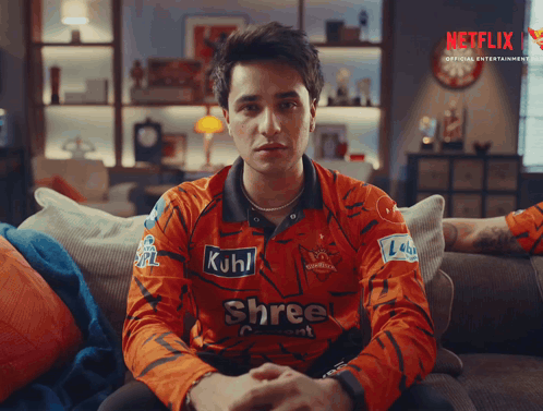 A Man Is Sitting On A Couch Wearing A Shree Shirt GIF