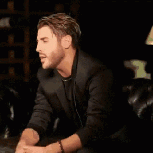 a man is sitting on a couch wearing headphones and a black jacket .