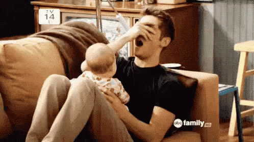 A Man Is Sitting On A Couch With A Baby And Drinking From A Bottle . GIF