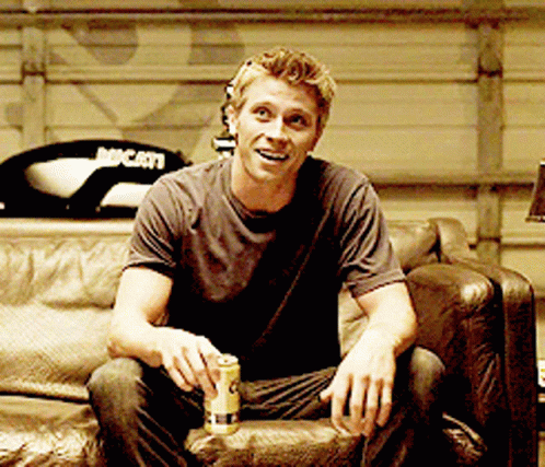 A Man Is Sitting On A Couch With A Can Of Beer And A Ducati Motorcycle In The Background GIF