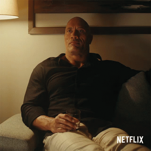 A Man Is Sitting On A Couch With A Glass Of Wine And A Netflix Logo On The Bottom GIF
