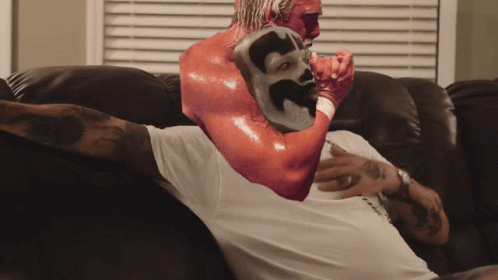 A Man Is Sitting On A Couch With A Red Mask On His Arm GIF
