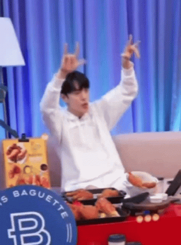 A Man Is Sitting On A Couch With His Arms In The Air And Making A Horn Sign . GIF