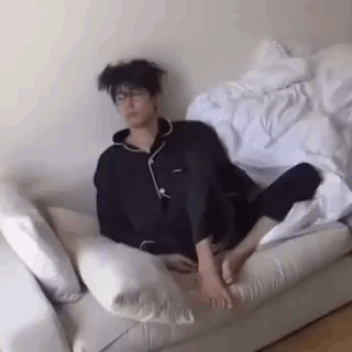 A Man Is Sitting On A Couch With His Feet Up And A Messy Haircut . GIF