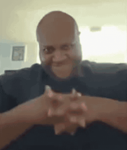 A Man Is Sitting On A Couch With His Hands Folded In Front Of His Face . GIF