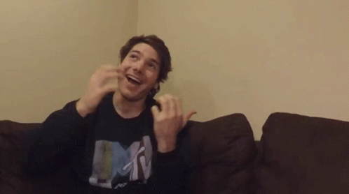 A Man Is Sitting On A Couch With His Hands In The Air And Wearing A Shirt That Says Mtv . GIF