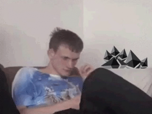 A Man Is Sitting On A Couch With His Legs Crossed And Looking At His Phone . GIF