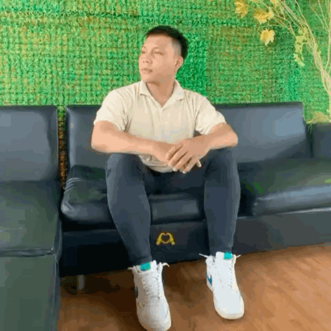 a man is sitting on a couch with his legs crossed and wearing white sneakers .