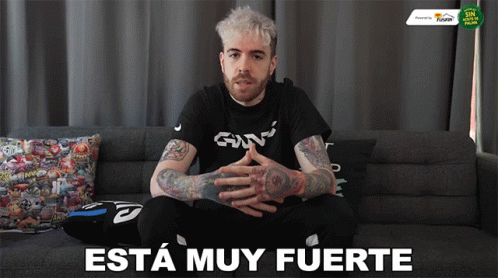 A Man Is Sitting On A Couch With The Words " Esta Muy Fuerte " Written On The Bottom GIF