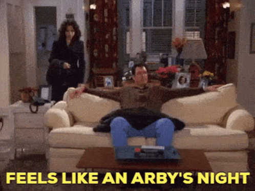 A Man Is Sitting On A Couch With The Words Feels Like An Arby 'S Night Behind Him GIF