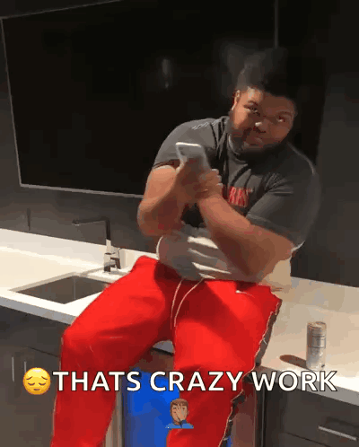 A Man Is Sitting On A Counter Looking At His Phone With The Words Thats Crazy Work Above Him GIF