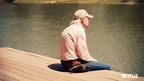 A Man Is Sitting On A Dock With A Netflix Logo Behind Him GIF