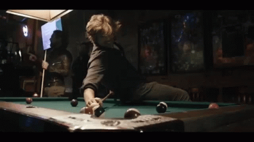 A Man Is Sitting On A Pool Table With A Pool Cue GIF