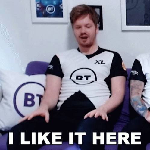 A Man Is Sitting On A Purple Couch With The Words I Like It Here On The Bottom GIF
