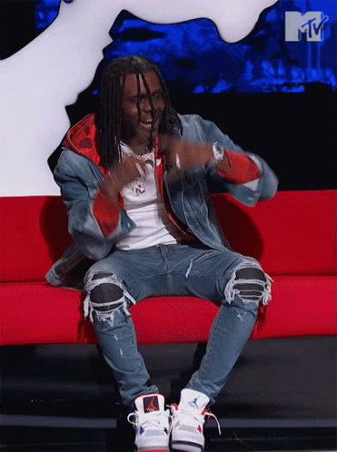 A Man Is Sitting On A Red Couch In Front Of A Mtv Sign GIF