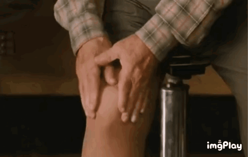 A Man Is Sitting On A Stool And Touching His Knee With His Hands . GIF