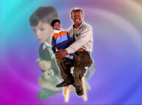 A Man Is Sitting On A Stool Holding A Puppet In His Lap GIF