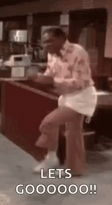 A Man Is Sitting On A Stool In Front Of A Counter And Dancing . GIF