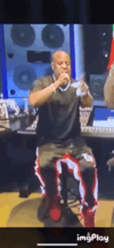 A Man Is Sitting On A Stool Singing Into A Microphone In A Recording Studio . GIF
