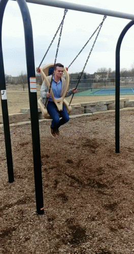 A Man Is Sitting On A Swing With A Warning Sign On It GIF