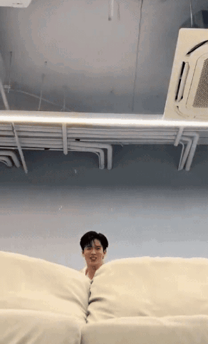 A Man Is Sitting On A White Couch In A Room With A Ceiling Fan . GIF