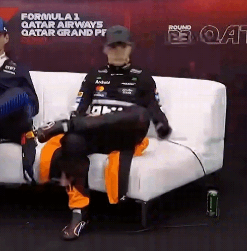A Man Is Sitting On A White Couch In Front Of A Sign That Says Formula 1 Qatar Airways GIF