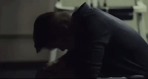 A Man Is Sitting On The Floor In A Dark Room Looking Down . GIF