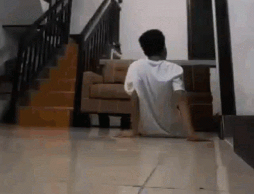 A Man Is Sitting On The Floor In A Living Room In Front Of A Staircase . GIF