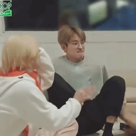 A Man Is Sitting On The Floor With His Legs Crossed And Another Man Is Sitting Next To Him . GIF
