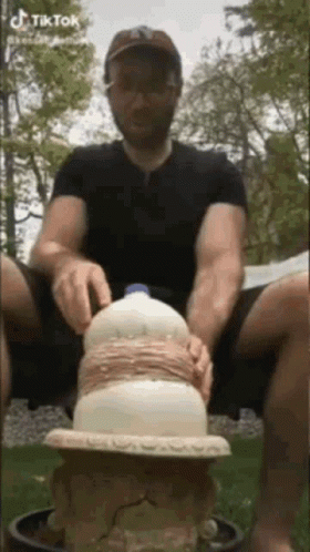 A Man Is Sitting On The Ground With A Milk Bottle On Top Of Him . GIF