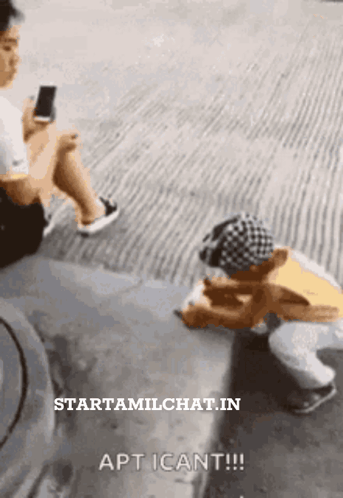 A Man Is Sitting On The Side Of The Road Looking At A Cell Phone GIF