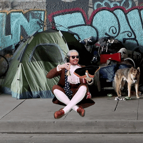A Man Is Sitting On The Sidewalk In Front Of A Tent With The Word N On It GIF