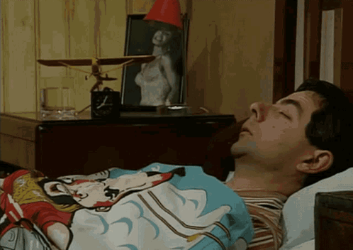 A Man Is Sleeping In A Bed With A Mickey Mouse Blanket On GIF
