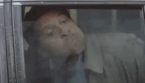 A Man Is Sleeping In A Car With His Mouth Open And His Tongue Sticking Out . GIF