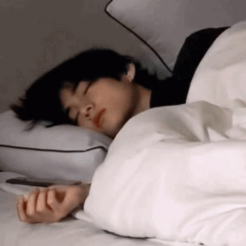 A Man Is Sleeping On A Bed With A White Blanket And Pillows . GIF